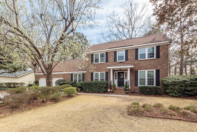 colonial inspired home featuring brick siding, an attached garage, and a front yard