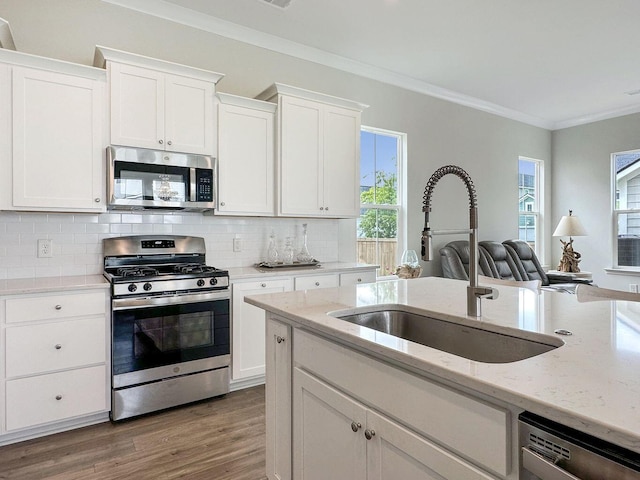 kitchen with a sink, white cabinetry, ornamental molding, appliances with stainless steel finishes, and decorative backsplash