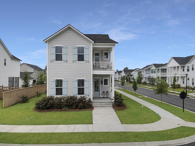 view of front of house with a front yard, a residential view, a balcony, and fence