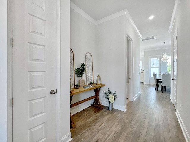 hallway with baseboards, visible vents, wood finished floors, an inviting chandelier, and crown molding