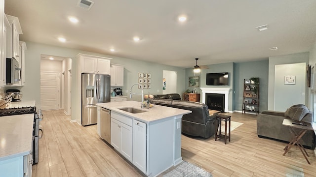 kitchen with sink, white cabinetry, stainless steel appliances, light hardwood / wood-style floors, and a center island with sink