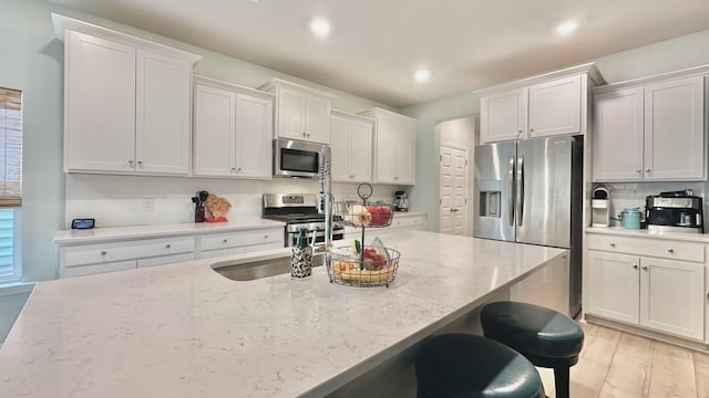 kitchen featuring white cabinetry, light stone countertops, stainless steel appliances, and a kitchen breakfast bar