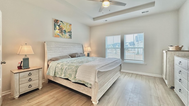 bedroom with a raised ceiling, ceiling fan, and light wood-type flooring