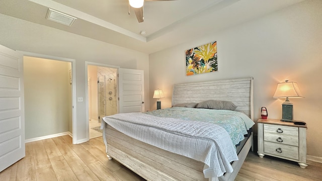 bedroom with ceiling fan, connected bathroom, light wood-type flooring, and a tray ceiling