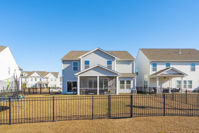 rear view of house featuring a trampoline, a residential view, a sunroom, and a fenced backyard