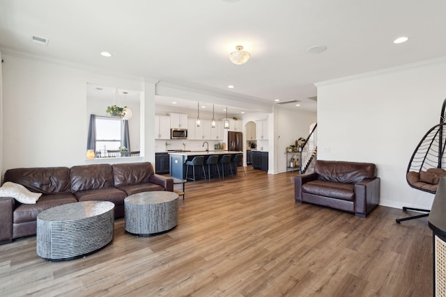 living room featuring recessed lighting, crown molding, light wood finished floors, and stairs