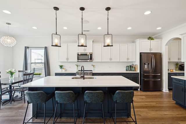 kitchen featuring light countertops, appliances with stainless steel finishes, an island with sink, and decorative light fixtures