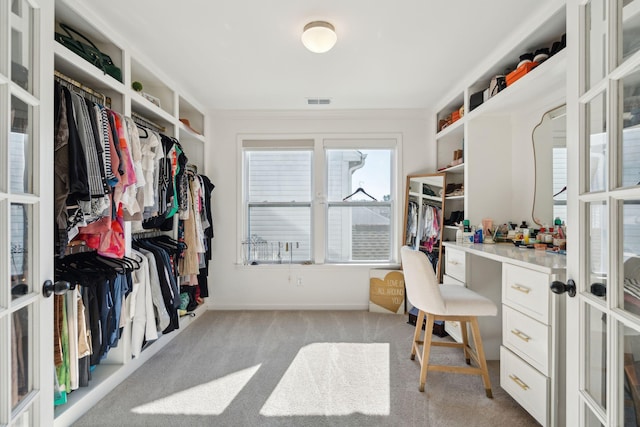 spacious closet with french doors, built in study area, and light colored carpet