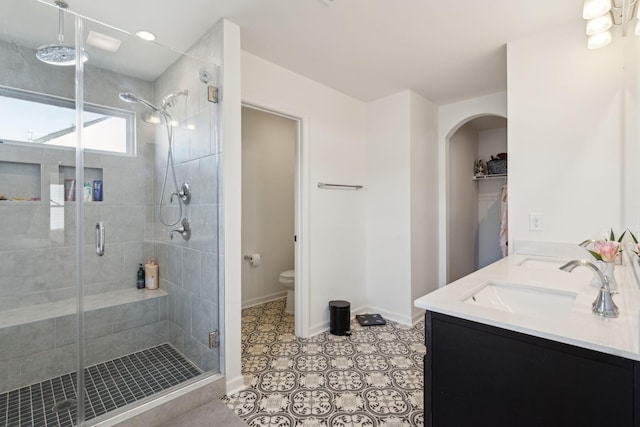 full bathroom featuring double vanity, baseboards, toilet, a shower stall, and a sink