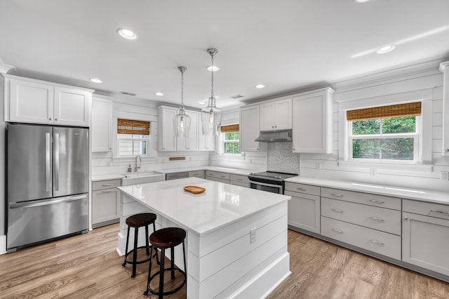 kitchen with stainless steel appliances, tasteful backsplash, light countertops, light wood-type flooring, and under cabinet range hood