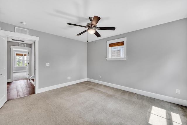 carpeted empty room with visible vents, ceiling fan, and baseboards