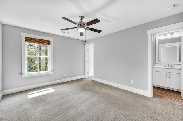 unfurnished bedroom featuring carpet floors, visible vents, ensuite bathroom, a sink, and baseboards