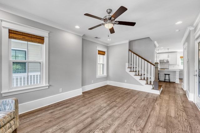 unfurnished living room featuring ornamental molding, stairway, baseboards, and wood finished floors