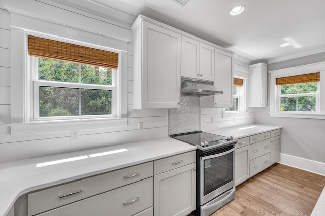 kitchen featuring light wood finished floors, light countertops, backsplash, stainless steel range with electric cooktop, and under cabinet range hood