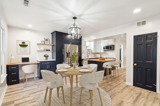 dining room with light wood-type flooring, a notable chandelier, and sink