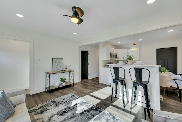 kitchen with ceiling fan, dark hardwood / wood-style floors, pendant lighting, white cabinets, and a breakfast bar