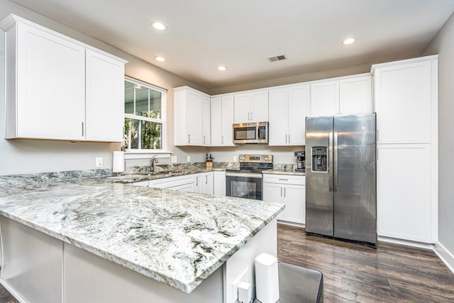 kitchen featuring white cabinetry, dark hardwood / wood-style flooring, kitchen peninsula, stainless steel appliances, and light stone counters