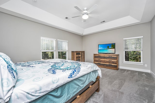 carpeted bedroom with a raised ceiling and ceiling fan