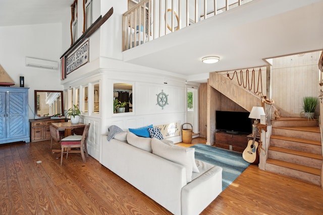 living room featuring a towering ceiling, wood-type flooring, and an AC wall unit