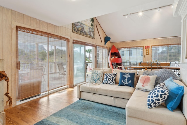 living room featuring track lighting, hardwood / wood-style floors, wooden walls, and lofted ceiling