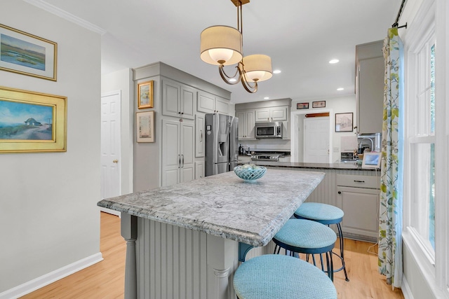 kitchen featuring stainless steel appliances, light wood-type flooring, gray cabinets, and a breakfast bar area