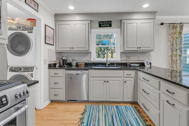 kitchen featuring stacked washer and dryer, ornamental molding, stainless steel appliances, and a sink