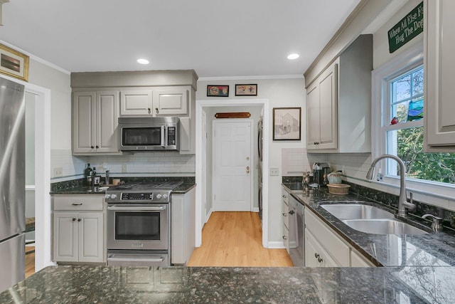 kitchen with dark stone countertops, appliances with stainless steel finishes, a sink, and ornamental molding