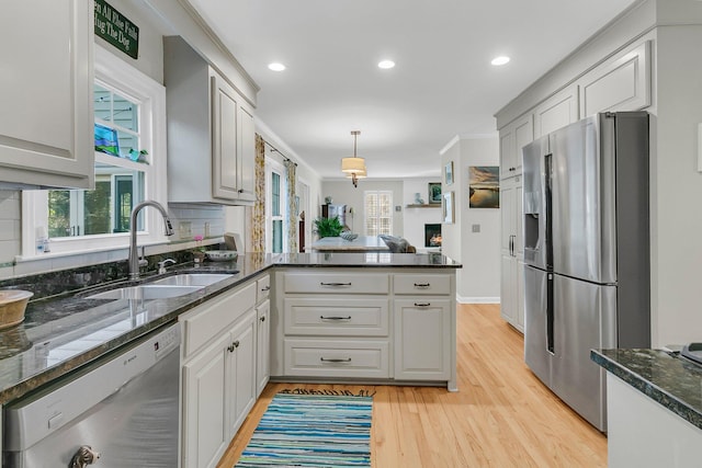 kitchen with light wood-style flooring, a peninsula, a sink, hanging light fixtures, and appliances with stainless steel finishes