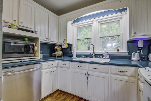 kitchen with dark countertops, appliances with stainless steel finishes, wood finished floors, white cabinetry, and a sink