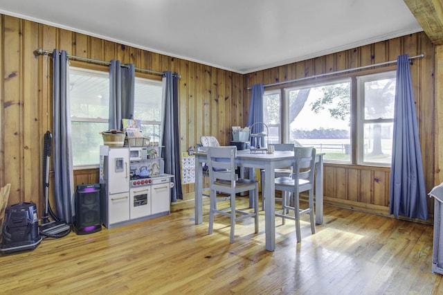 dining area featuring wooden walls, a healthy amount of sunlight, ornamental molding, and light wood-style flooring