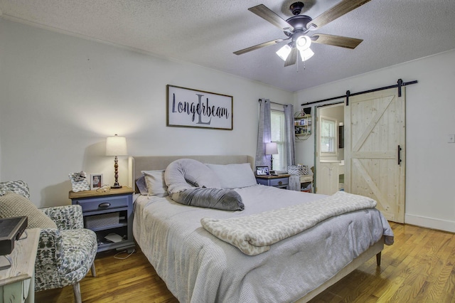 bedroom featuring a textured ceiling, ceiling fan, a barn door, and wood finished floors