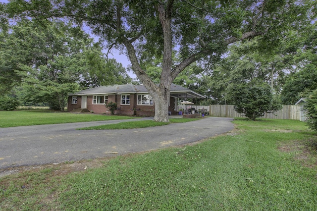 ranch-style home with brick siding, fence, driveway, and a front lawn