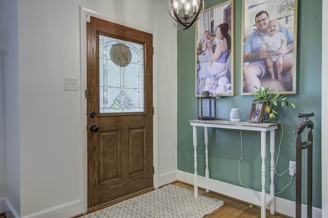 foyer entrance with an inviting chandelier, baseboards, and wood finished floors