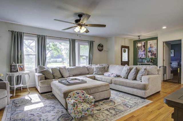 living area with light wood-type flooring, recessed lighting, and ceiling fan with notable chandelier