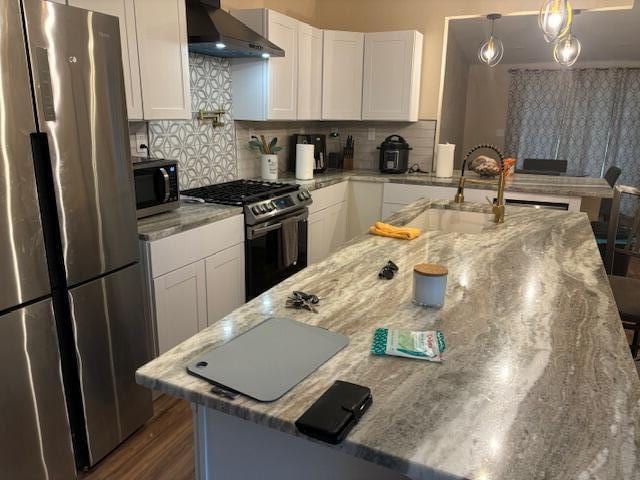 kitchen featuring light stone countertops, decorative backsplash, wall chimney range hood, white cabinetry, and appliances with stainless steel finishes