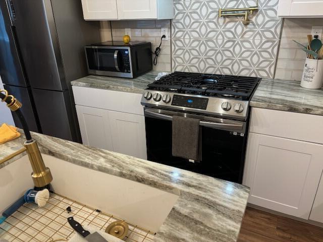 5309 Good St, North Charleston, SC 29406 - kitchen with stainless steel gas range oven, freestanding refrigerator, black microwave, backsplash, and white cabinets