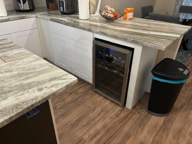 bar with light stone countertops, wine cooler, white cabinetry, and dark hardwood / wood-style floors