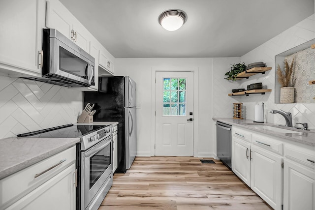 kitchen featuring stainless steel appliances, tasteful backsplash, a sink, white cabinets, and light wood-type flooring