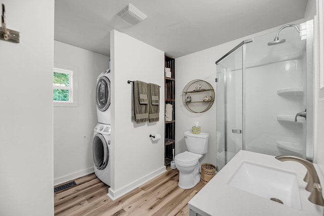 bathroom featuring stacked washer / dryer, wood finished floors, a shower stall, a sink, and toilet