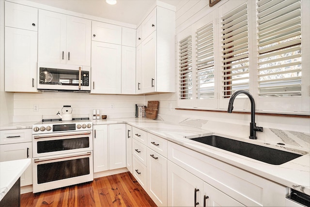 kitchen with white cabinetry, sink, white appliances, and hardwood / wood-style flooring