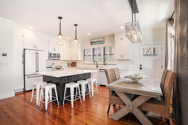 kitchen featuring a breakfast bar, hanging light fixtures, a kitchen island, white appliances, and white cabinets