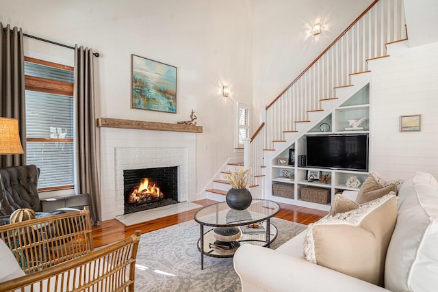 living room featuring hardwood / wood-style floors, built in shelves, a fireplace, and a towering ceiling