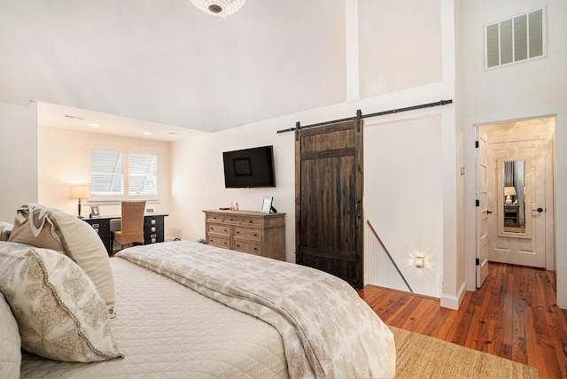 bedroom with a barn door, dark hardwood / wood-style flooring, and a high ceiling