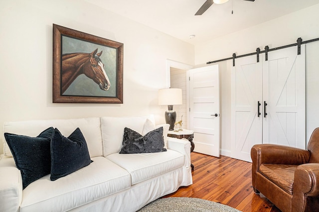 living room with wood-type flooring, a barn door, and ceiling fan