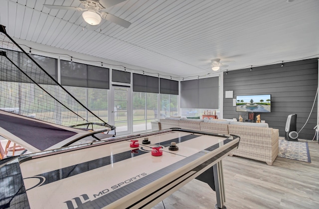 game room featuring light hardwood / wood-style floors, wood walls, and ceiling fan