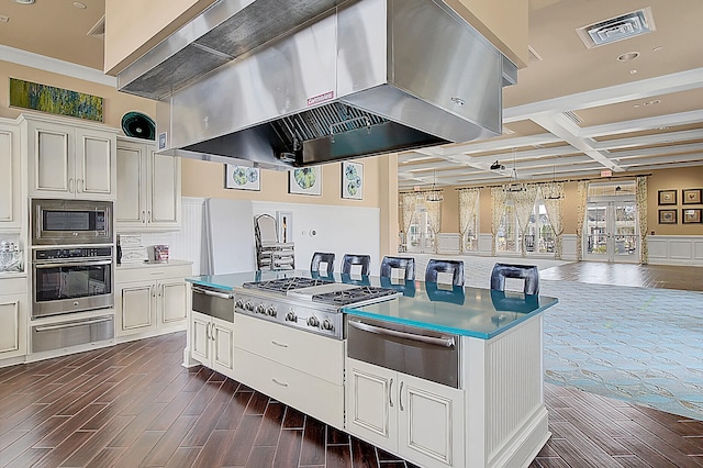 kitchen with coffered ceiling, beamed ceiling, wall chimney range hood, white cabinetry, and appliances with stainless steel finishes