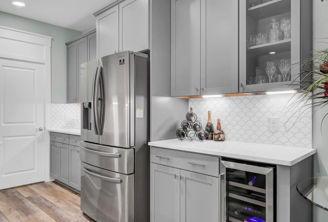 kitchen with beverage cooler, gray cabinets, stainless steel fridge, light wood-type flooring, and decorative backsplash