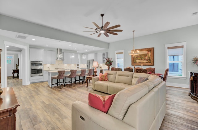 living room featuring ceiling fan with notable chandelier and light wood-type flooring