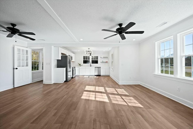 unfurnished living room with dark wood-type flooring, ceiling fan with notable chandelier, visible vents, and baseboards