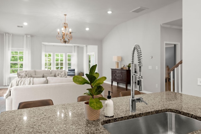 kitchen with vaulted ceiling, sink, pendant lighting, stone countertops, and an inviting chandelier